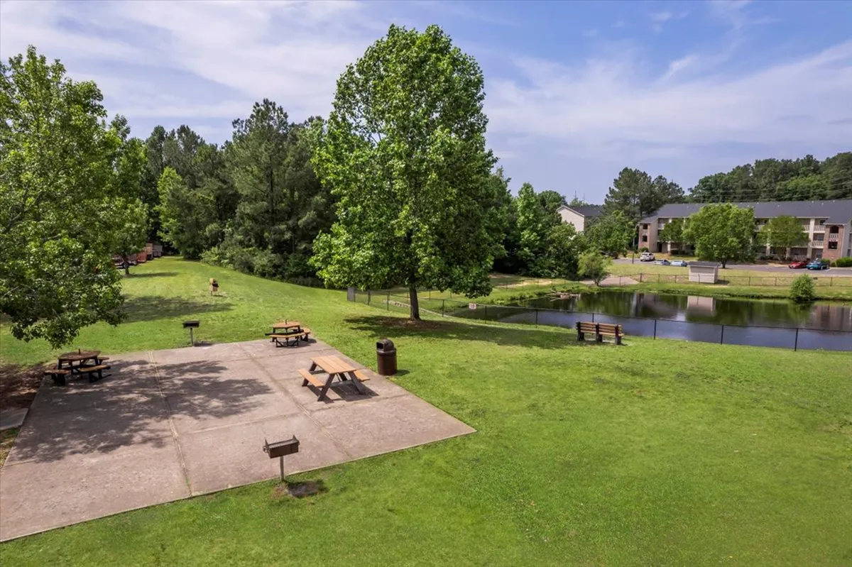 This tranquil park-like setting offers large trees for shade, picnic tables overlooking a peaceful pond, benches for relaxing, and open grassy areas—ideal for family outings, picnics, or quiet reflection.