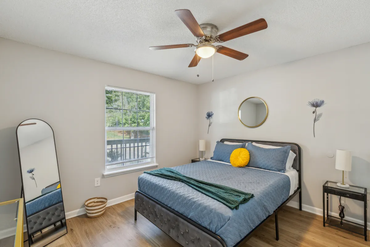 A beautifully styled bedroom featuring a plush bed adorned with soft linens, flanked by modern nightstands and elegant lamps. A large mirror reflects the calming decor and decorative wall art, while gentle natural light streams in, creating a warm and inviting atmosphere perfect for relaxation.