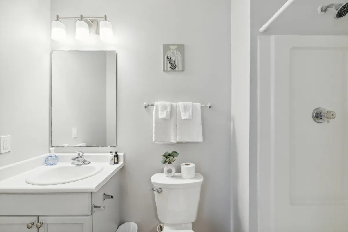 A stylish bathroom with a well-lit sink and mirror, fluffy towels, a modern shower area, and a decorative plant. The space feels calm and inviting, ideal for relaxing showers or morning routines.